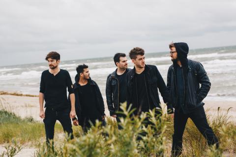 Die fünf Jungs von Antiheld stehen auf einer Düne. Im Hintergrund ist das Meer zu sehen.